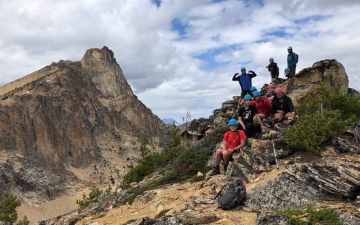 a group of students smile for a photo at the summit of a mountain